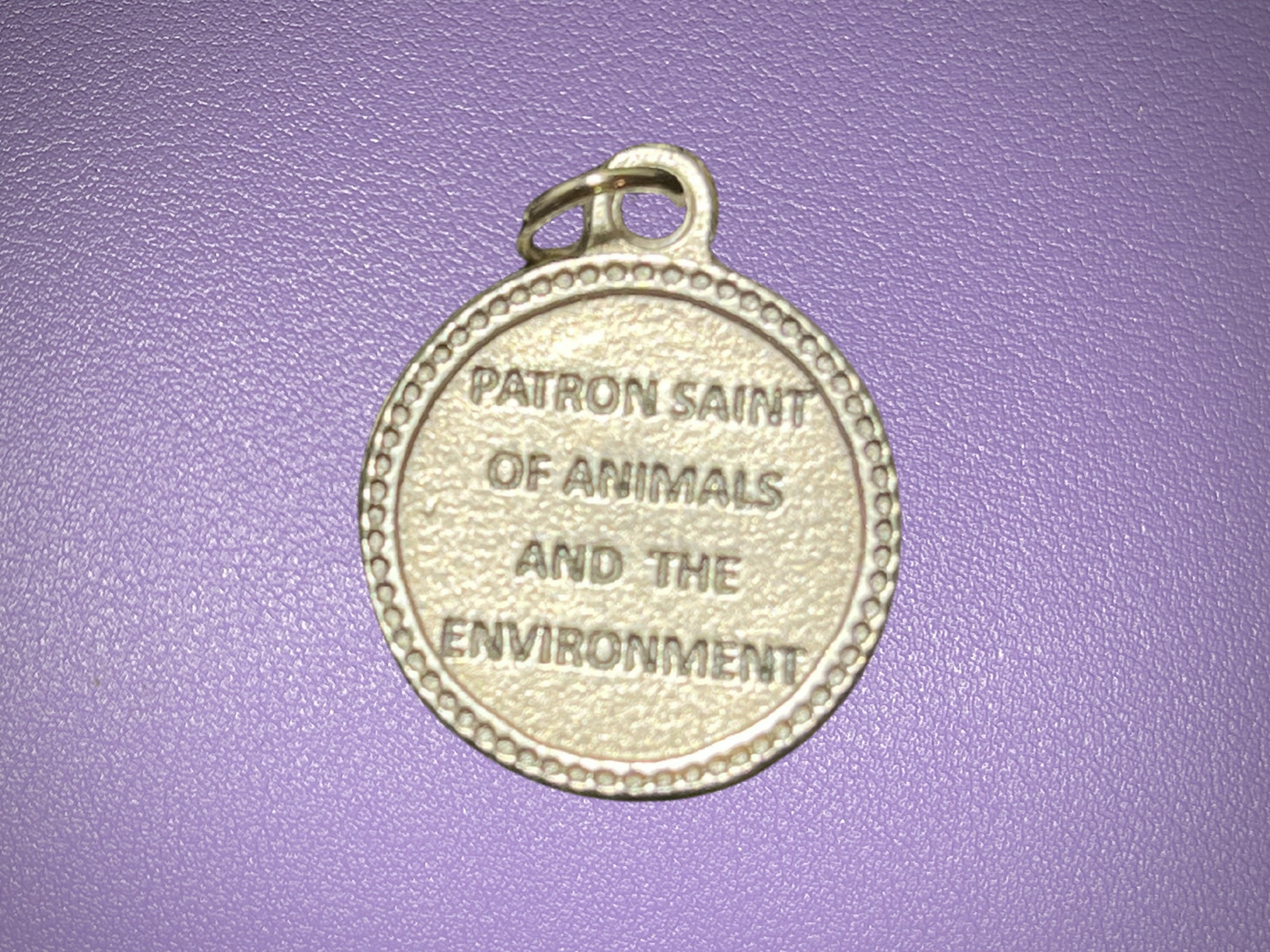 Medal with 'Patron Saint of Animals and the Environment' text on a purple background